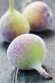 Three whole figs on a green wooden surface