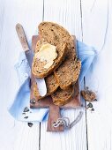 Roggenbrotscheiben, eine davon mit Butter, auf Schneidebrett