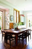 Dunkle Holzstühle um Tisch auf rustikalem Dielenboden in Wohnküche mit pastellfarbenen Wänden