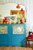 Blau lackierter halbhoher Schrank mit bedrucktem Papier hinter Türglas im Kinderzimmer