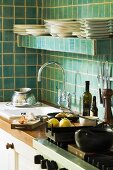 Küchenecke - Küchenzeile mit Spüle und Herd unter Ablage mit Geschirr vor grün gefliester Wand