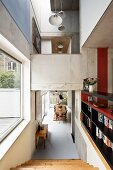 Open-plan, multi-level interior with exposed concrete; pale wooden stairs in foreground leading to dining area