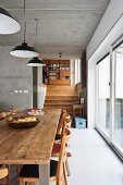 Rustic dining table and chairs next to floor-to-ceiling glass wall; three simple metal lampshades hanging from ceiling