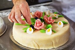 A confectioner decorating a marzipan layer cake with marzipan flowers