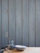 Teller, Glas und Tuch auf Holztisch vor grauer Holzwand