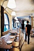 Two waiters walking through restaurant with set wooden tables