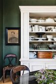 Crockery in white-painted dresser behind flowers on partially visible table in traditional dining room