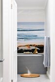 View through open door into bathroom; poster with beach and ocean motif above bathtub