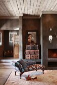 Antique chaise longue on rug in front of open fireplace and animal trophies on wall in rustic, country-house living room