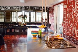 Kitchen counter with gas hob in modern interior with stencilled pictures on wall; ribbon window with closed shutters in background