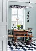 Antique, Biedermeier-style table and chairs below old hunting horn hanging in kitchen window; black and white gingham pelmet and chequered floor