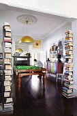 View of man playing billiards through wide open doorway flanked by stacks of books