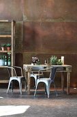 Rustic dining table made from pallet, metal chairs and partially visible shelving against corten steel wall