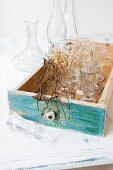 Old stemware in vintage drawer with front painted blue-green; collection of glass carafes in background