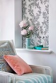 Pastel pink cushion on white cane armchair with white frame next to wall with bouquet in wallpapered niche