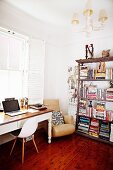 Bauhaus chair and desk below window next to armchair and antique bookcase in corner