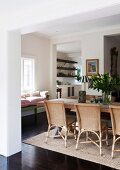 Pleasant dining area with wicker chairs and wooden table on sisal rug; window seat with many cushions in background