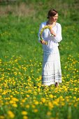 Junge Frau in Löwenzahnwiese mit Blumenkranz in der Hand