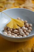 Gingko nuts and a yellow gingko leaf in a porcelain bowl