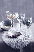Craft beads in silver dishes and wine glasses on lace doily