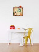 An die Wand gehängte Holzkiste mit gemusterter Rückwand für Bücher, Stifte und Deko-Utensilien; kleiner Schreibtisch mit gelbem Retro-Metallstuhl