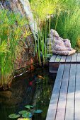 Stone figure at end of wooden jetty next to pond with aquatic plants