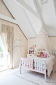 Vintage child's bed with canopy hanging from sloping attic ceiling next to window with gathered curtain
