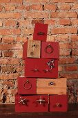Stacked boxes, some painted rust red, with attached components against rustic brick wall