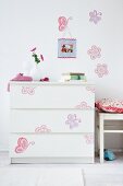 Colourful decals on simple, white chest of drawers and wall