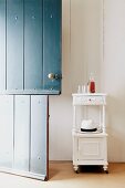 White-painted wooden side table with turned pillars and carved ornamentation against wall next to blue wooden stable door