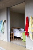 Farbige Strandtücher an einer Flurwand aufgehängt und Blick durch geöffnete Schiebetür auf Schlafraum mit Doppelbett