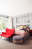 Roter Loungesessel und Sitzpolster vor Bett an Wand mit Ornamentmuster auf Tapete in modernem Schlafzimmer mit Retroflair