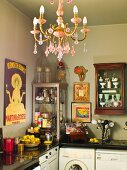 Küchenecke mit Vitrinen und antiquarischem Geschirr über Arbeitsplatte, im Vordergrund Kronleuchter mit rosa Glasschmuck