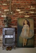 Vintage Ventilator auf antikem, Metallschränkchen und Ölgemälde vor rustikaler Ziegelwand im Wohnbereich