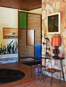 Diele im 50er Jahrestil mit Natursteinwand, Raumteiler mit farbigen Glaseinsätzen und Deko im Folklorestil; Patchworkteppiche aus dunklem Leder