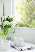 Breakfast for one - coffee cup on folded newspaper next to bouquet of white hyacinths in glass vase in front of vintage window