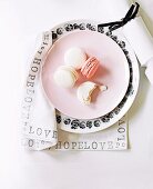Place setting with macaroons on pink dessert plate and black and white floral plate on napkin printed with black lettering