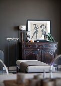 Various artworks and sculptures on antique cabinet against dark-painted wall; ottoman and Ghost chairs in foreground