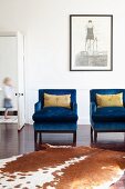 Animal-skin rug in front of bright blue armchairs and artwork on wall; door to one side