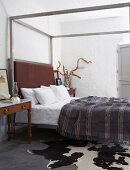 Simple bedroom with striped blanket on canopied bed; animal-skin rug on floor in foreground