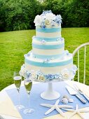 Blue and White Wedding Cake with Two Glasses of Champagne and Sea Shells on an Outdoor Table