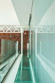 Loft gallery with glass floor and balustrade, steel joist structure against brick wall at far end and glass wall to one side