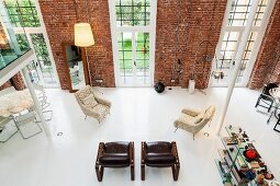 Blick von Loftgalerie auf grosszügig verteilte Sessel und Designer Stehleuchten vor Backsteinwand mit raumhohen Fenstern