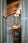 View into grey-tiled bathroom with rustic wooden washstand, mirror and sconce lamps