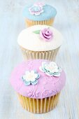 Three pastel-coloured cupcakes with glacé icing and sugar flowers