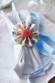 Colourful paper rosette with red button on pale blue ribbon as napkin ring tying napkin and cutlery