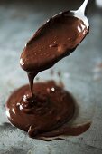 Liquid chocolate dripping off a spoon onto a baking tray