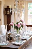 Mit viel Gläsern, silbernen Kerzenleuchtern und zartem Pfingstrosenstrauss festlich gedeckter Tisch in gediegenem Esszimmer