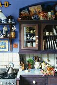 Geflieste Küchenzeile mit Unterschrank und Hängeschränke mit Geschirr an blauer Wand in ländlicher Küche