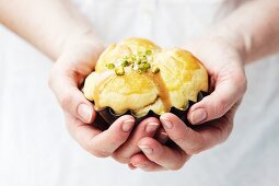 A woman's hands holding a brioche with caramel sauce and pistachios